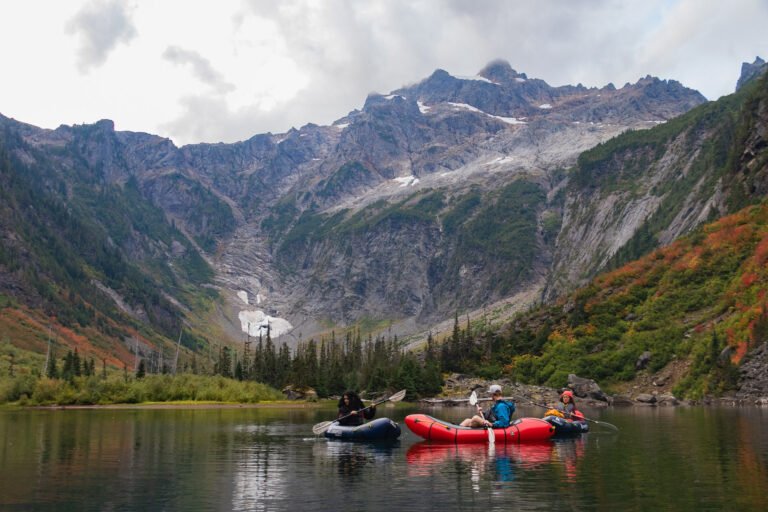 Three people packrafting on an alpine lake in Washington with a mountain in the background, showcasing one of the best packrafting destinations in the world.