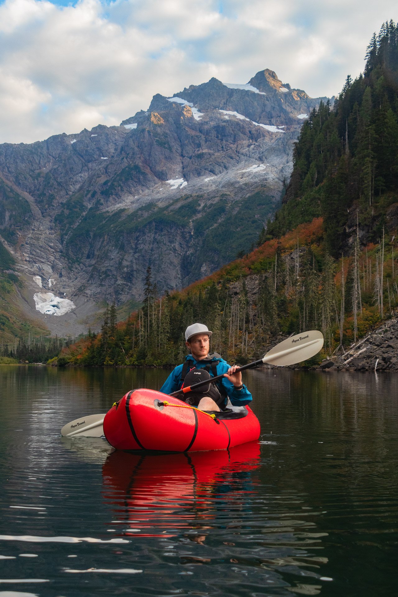 An image of the author packrafting on an alpine lake in Washington with a mountain peak behind, featured in the 'About Me' section.
