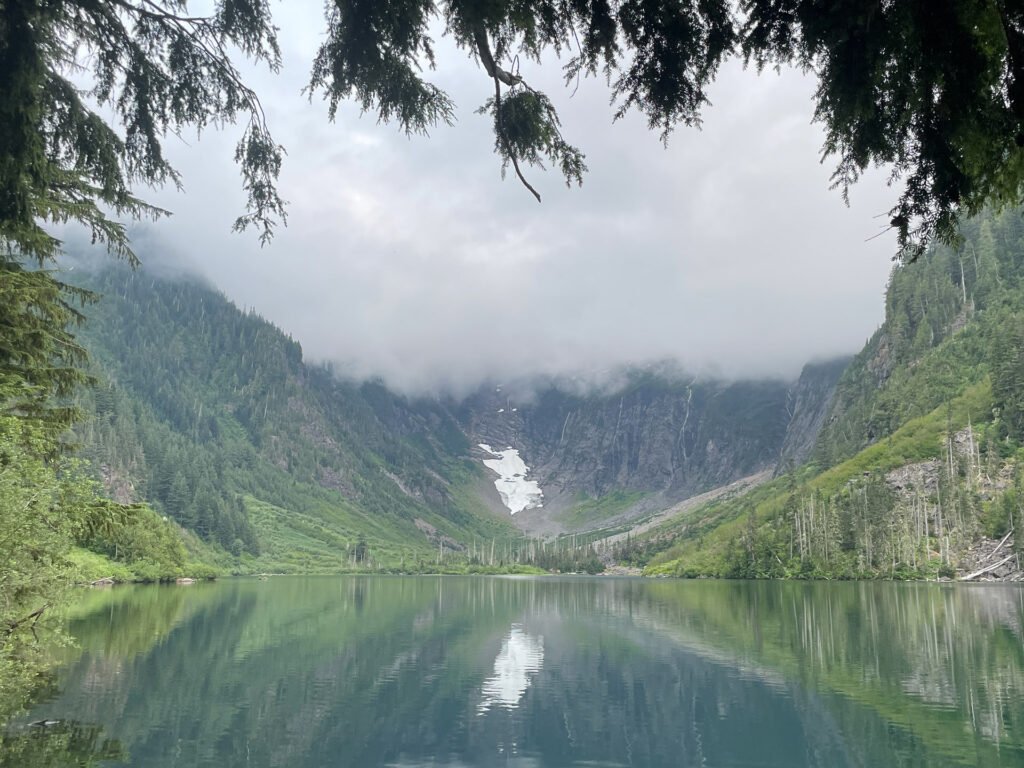 A fog-covered alpine lake in the Washington Cascades, featuring cascading waterfalls and a glacier-fed basin for a peaceful, remote adventure.