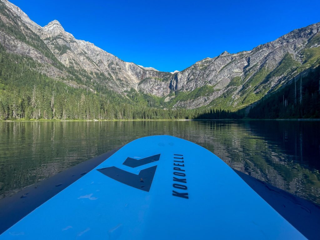 A packrafter’s perspective from the center of Avalanche Lake in Glacier National Park, surrounded by towering cliffs and pristine waters, showcasing how to avoid crowds in the outdoors.