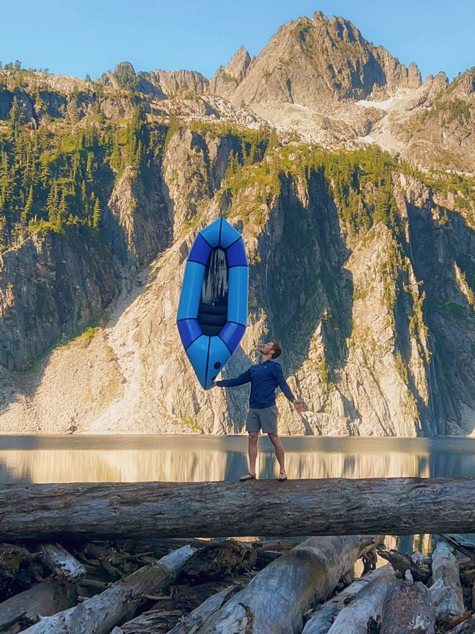 Adam Jones, owner and lead guide of Optimum Adventures, holding an Alpacka Scout packraft on one finger at Snow Lake, showcasing lightweight packrafting gear in Washington.