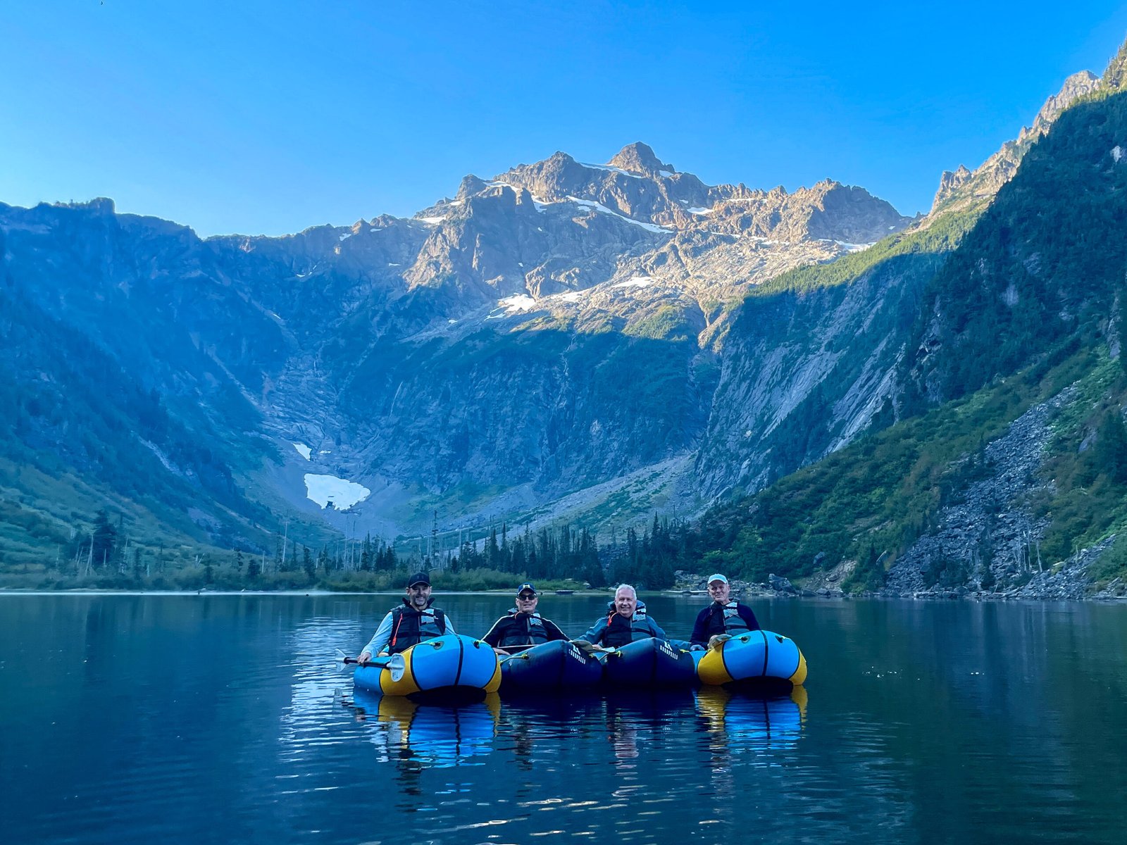 Four guests paddling Alpacka and Kokopelli packrafts on Goat Lake with North Cadet Peak, a glacier, and pristine water during the Optimum Adventures Goat Lake kayaking tour.