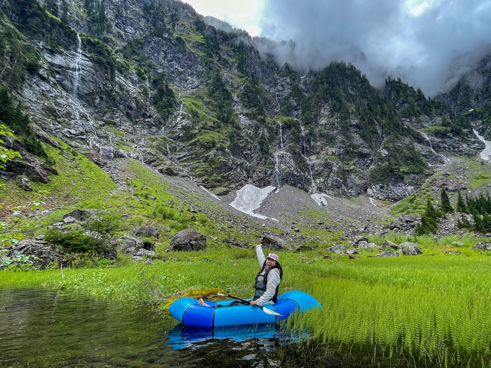 An excited guest posing in a packraft on beautiful Lake 22 during a guided alpine lake kayaking tour with Optimum Adventures.