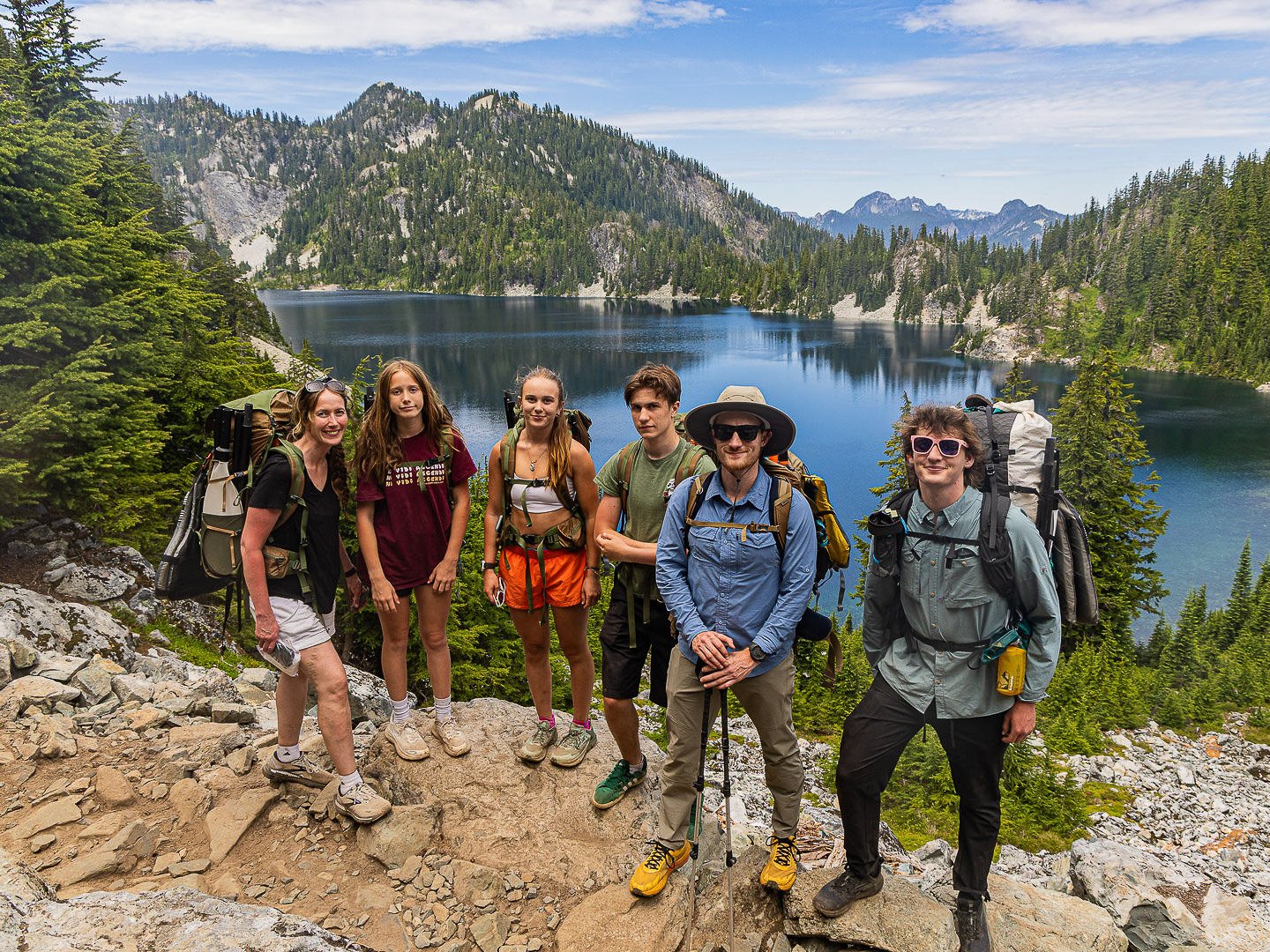 A family posing for a group photo beside Snow Lake with turquoise water and distant Cascade Mountains during the Optimum Adventures Snow Lake tour in Washington.
